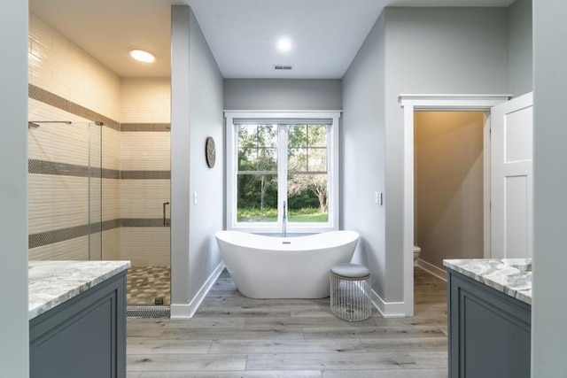 bathroom with wood finished floors, a freestanding bath, a stall shower, and vanity