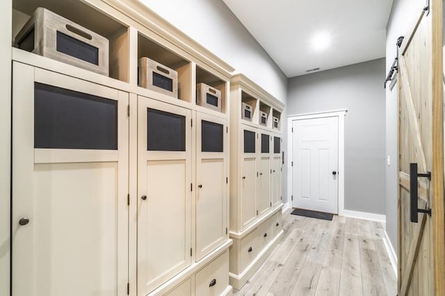 mudroom with a barn door, baseboards, and light wood finished floors