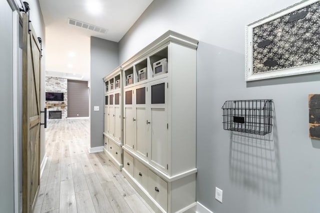 mudroom featuring light wood-type flooring, visible vents, a barn door, and baseboards