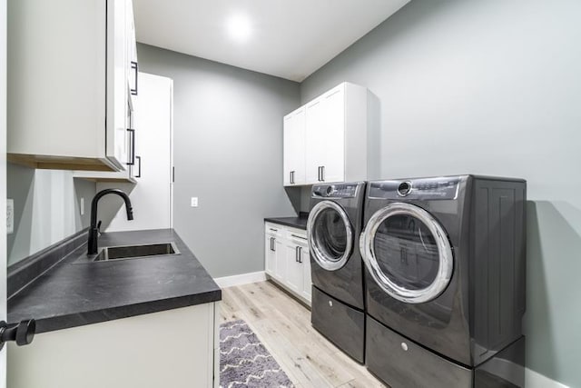 laundry room featuring baseboards, cabinet space, a sink, washing machine and dryer, and light wood-type flooring