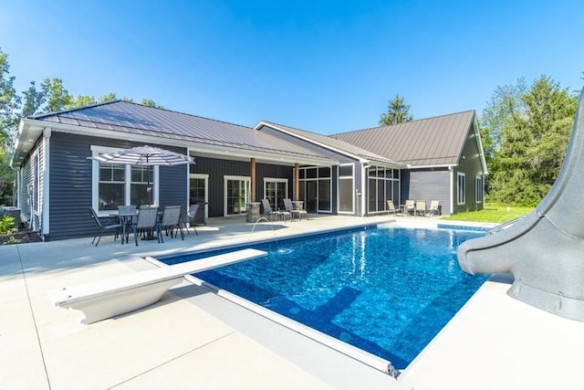 outdoor pool with a patio area, a diving board, and a water slide