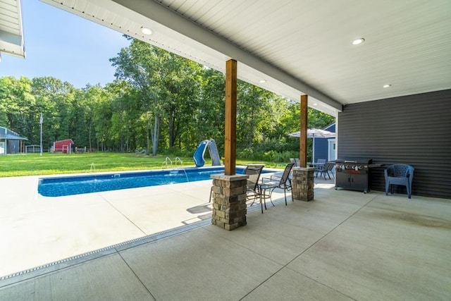 pool featuring a patio area, a lawn, a water slide, and an outbuilding