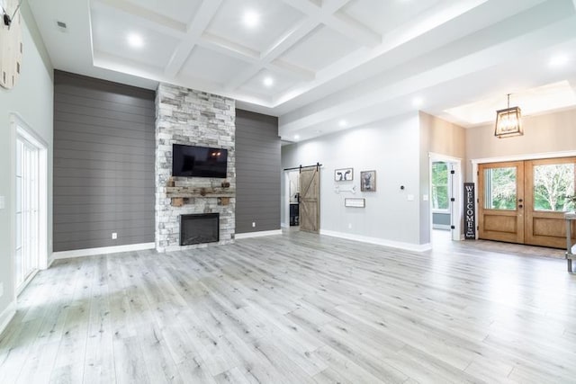 unfurnished living room featuring light wood-type flooring, beamed ceiling, coffered ceiling, a barn door, and a high ceiling