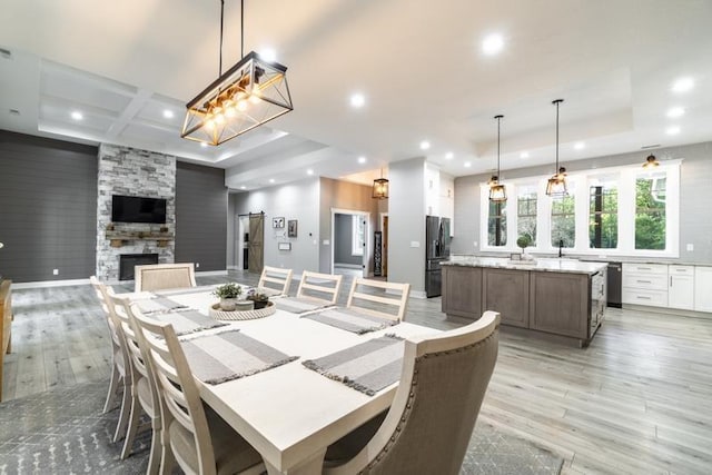 dining space with coffered ceiling, a tray ceiling, recessed lighting, a fireplace, and light wood-style floors