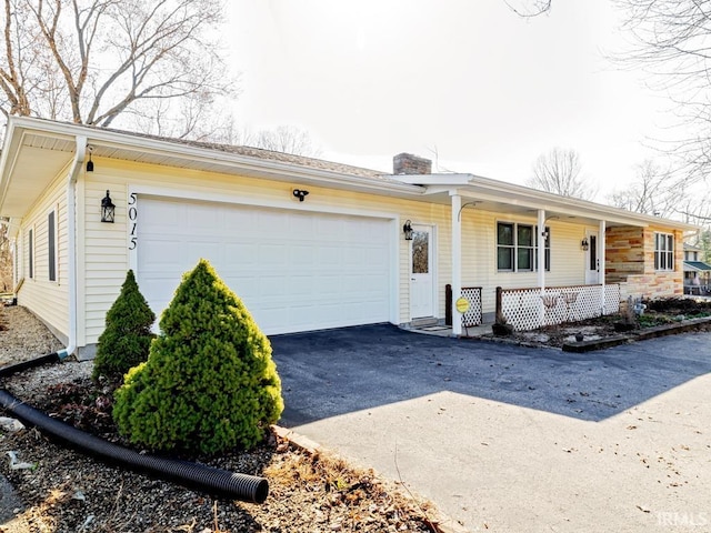 single story home featuring a garage, a porch, a chimney, and aphalt driveway