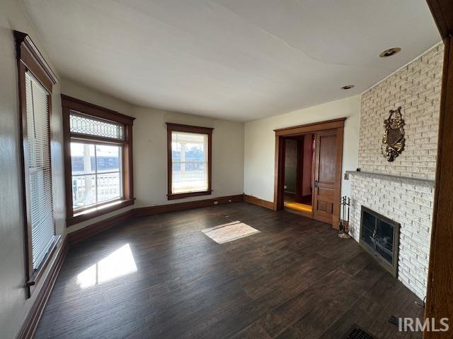 unfurnished living room featuring a fireplace, dark wood-style floors, and baseboards
