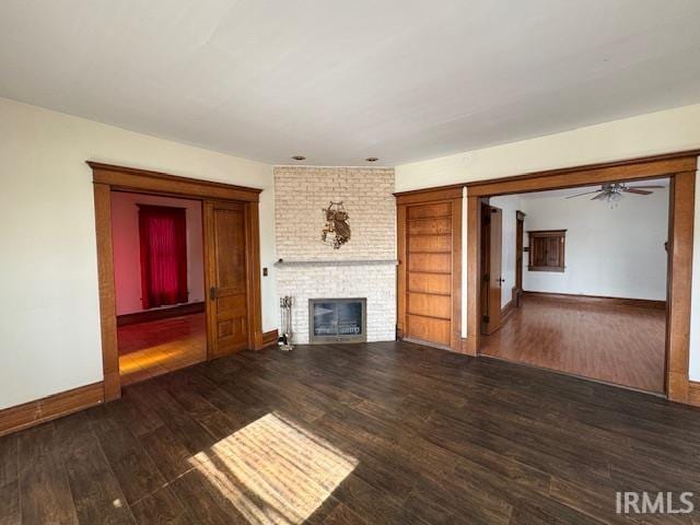 unfurnished living room with a brick fireplace, a ceiling fan, baseboards, and wood finished floors