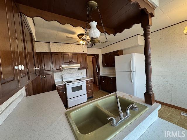 kitchen with under cabinet range hood, dark brown cabinetry, light countertops, white appliances, and a sink