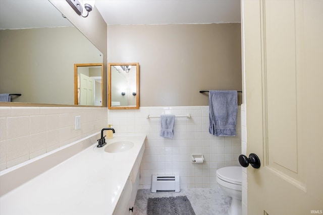 bathroom with toilet, a baseboard heating unit, tile walls, wainscoting, and vanity