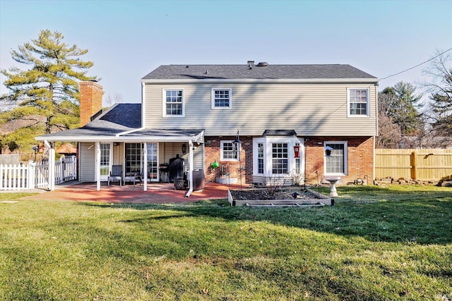 back of property featuring a yard, fence, brick siding, and a patio area