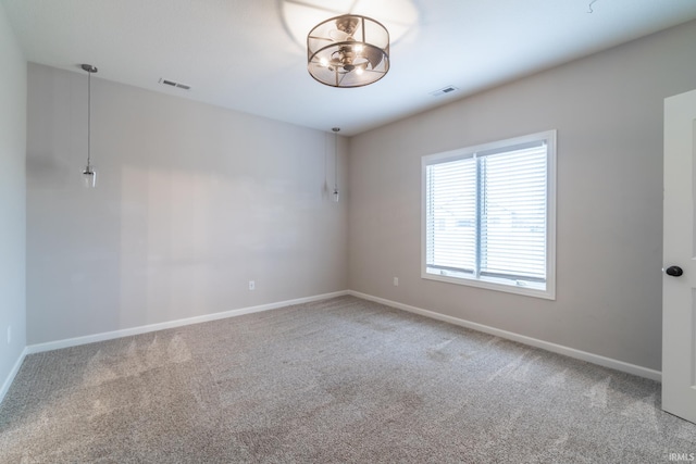 carpeted spare room with a chandelier, visible vents, and baseboards