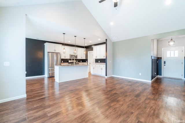 kitchen with open floor plan, dark wood-style floors, white cabinets, stainless steel appliances, and a kitchen island with sink