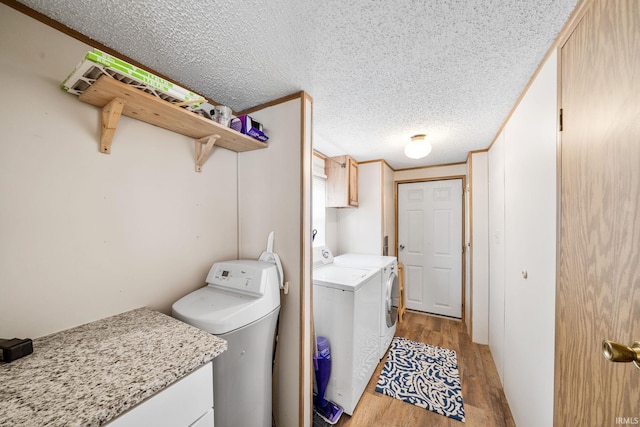 washroom with cabinet space, independent washer and dryer, light wood finished floors, and a textured ceiling