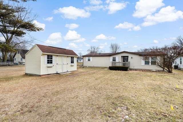 rear view of house featuring roof with shingles, central AC unit, a yard, an outdoor structure, and a storage unit