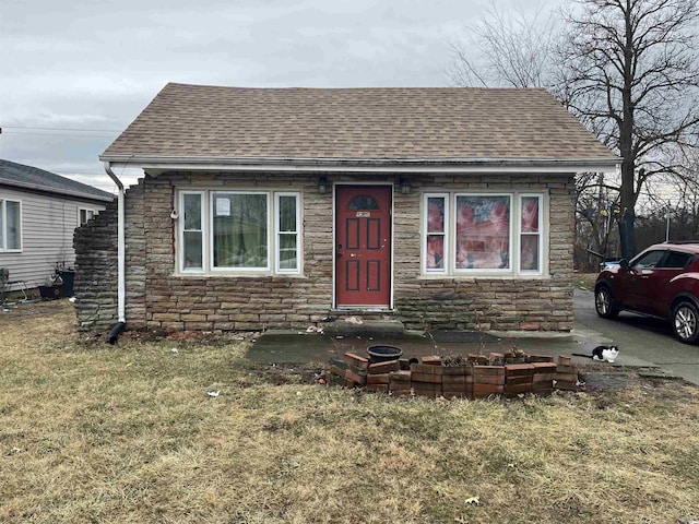 bungalow-style house with stone siding, a front yard, and roof with shingles