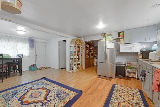 kitchen featuring white microwave, light wood-type flooring, freestanding refrigerator, and light countertops