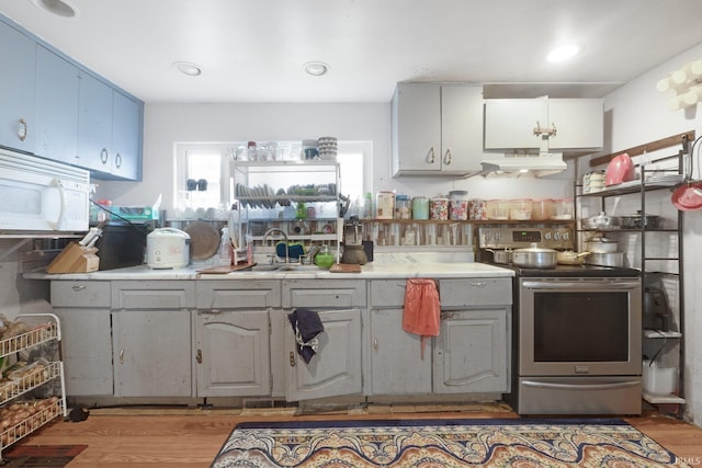 kitchen with stainless steel electric range oven, white microwave, a sink, light wood-style floors, and under cabinet range hood