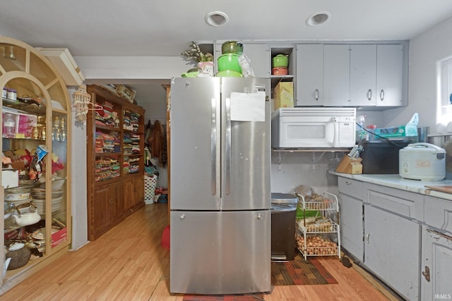 kitchen featuring white microwave, light countertops, freestanding refrigerator, and light wood-style floors