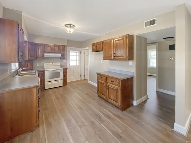 kitchen featuring light wood-type flooring, white electric range, under cabinet range hood, a sink, and light countertops