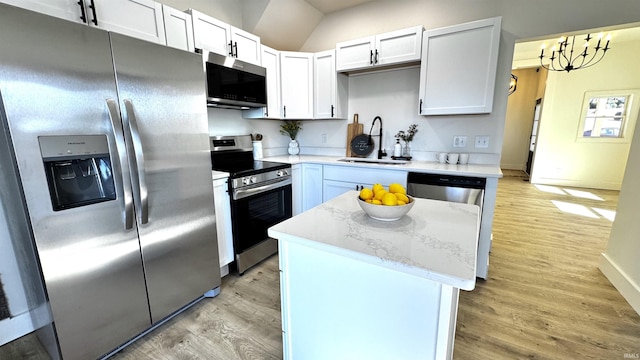 kitchen with a sink, a center island, stainless steel appliances, light wood-style floors, and light stone countertops