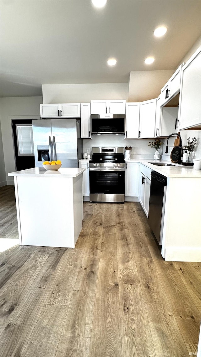 kitchen featuring wood finished floors, a kitchen island, recessed lighting, light countertops, and appliances with stainless steel finishes