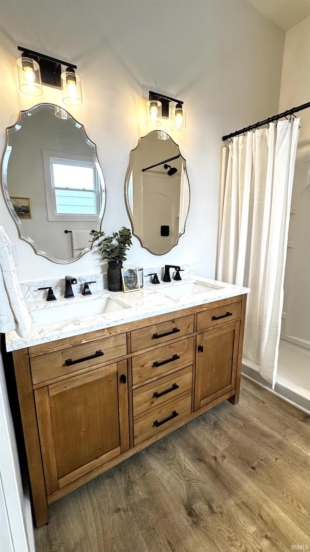 bathroom featuring curtained shower, double vanity, wood finished floors, and a sink