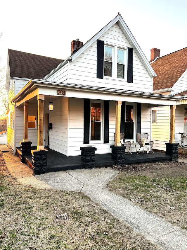 view of front facade with a shingled roof, a porch, and a chimney