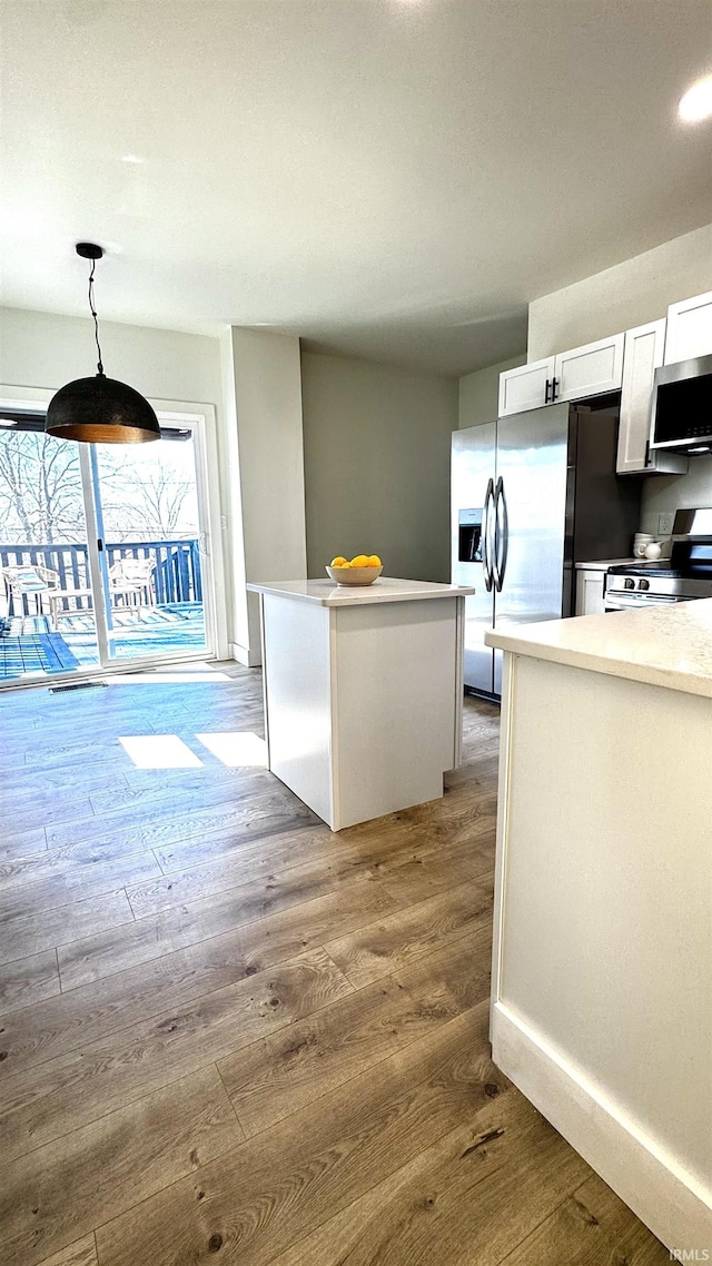 kitchen with light wood finished floors, white cabinets, appliances with stainless steel finishes, and decorative light fixtures