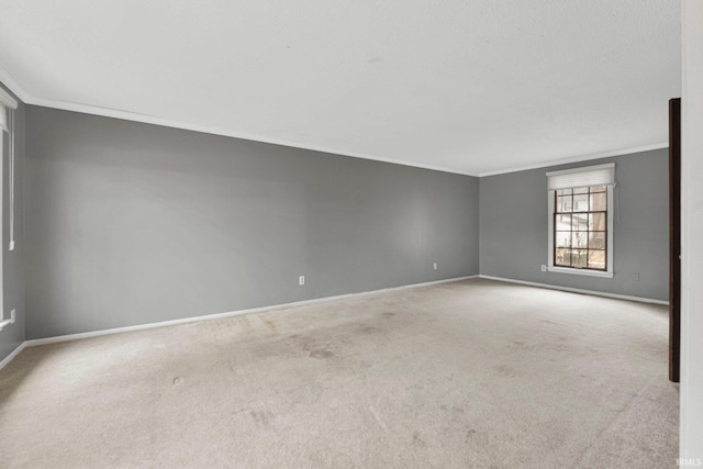 empty room with carpet flooring, crown molding, and baseboards