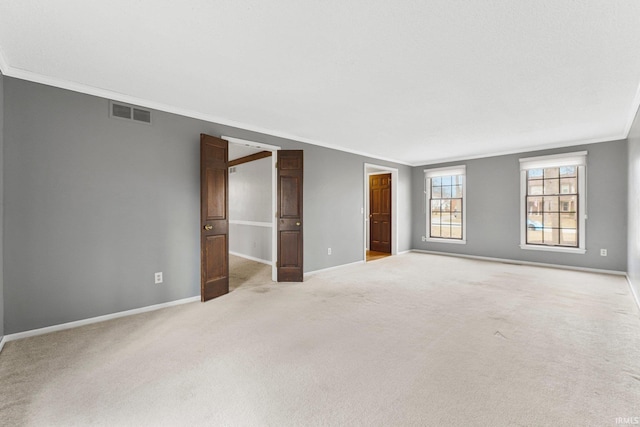 empty room featuring crown molding, light colored carpet, visible vents, and baseboards