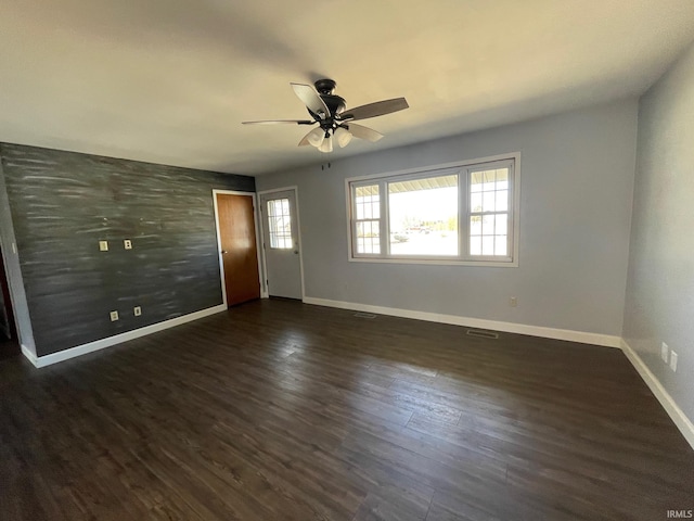 interior space with visible vents, baseboards, dark wood finished floors, ceiling fan, and an accent wall