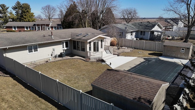 rear view of property with central air condition unit, a residential view, a fenced backyard, an outbuilding, and a storage unit