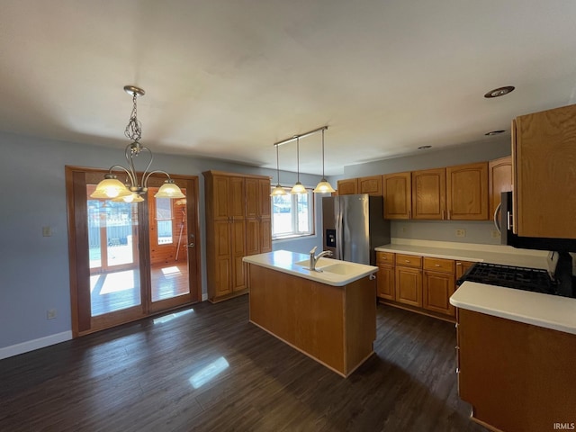 kitchen featuring an island with sink, stainless steel refrigerator with ice dispenser, decorative light fixtures, dark wood-style floors, and light countertops