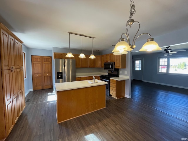 kitchen with dark wood-type flooring, a center island with sink, stainless steel appliances, light countertops, and hanging light fixtures