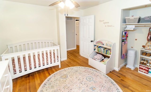 bedroom featuring a nursery area, wood finished floors, visible vents, and baseboards