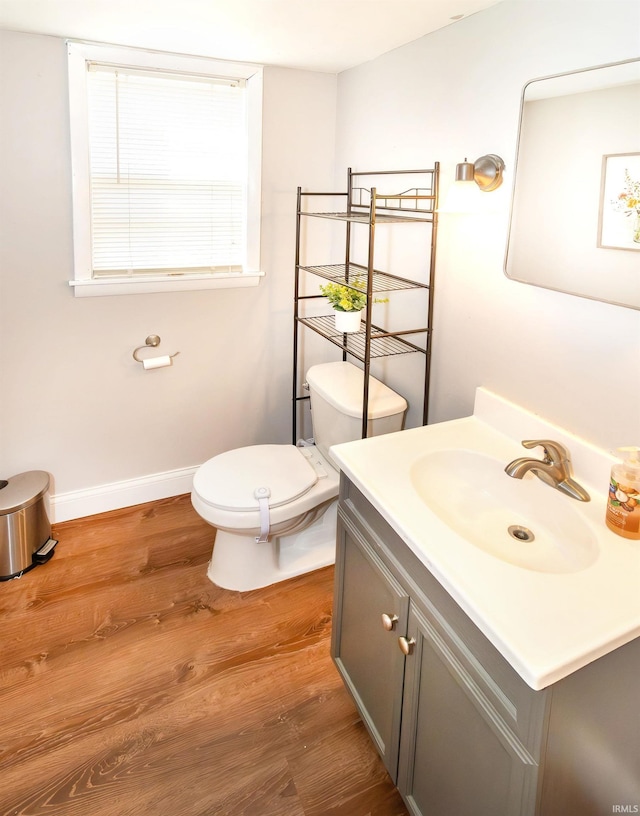 half bathroom featuring vanity, toilet, wood finished floors, and baseboards