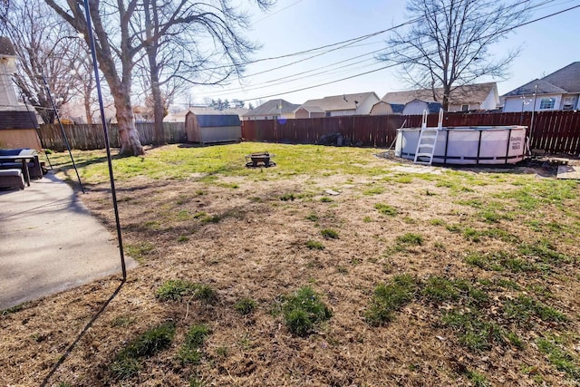 view of yard featuring an outbuilding, a fenced in pool, a fenced backyard, a storage unit, and a fire pit