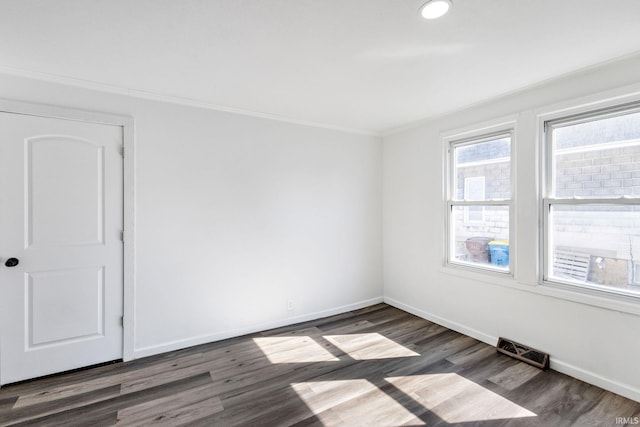 empty room with ornamental molding, wood finished floors, visible vents, and baseboards