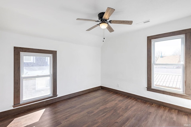 spare room with ceiling fan, visible vents, baseboards, and dark wood finished floors