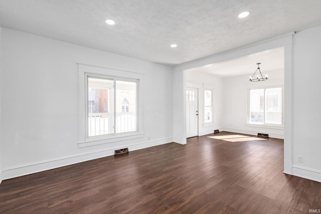 unfurnished living room featuring a wealth of natural light, visible vents, and dark wood finished floors