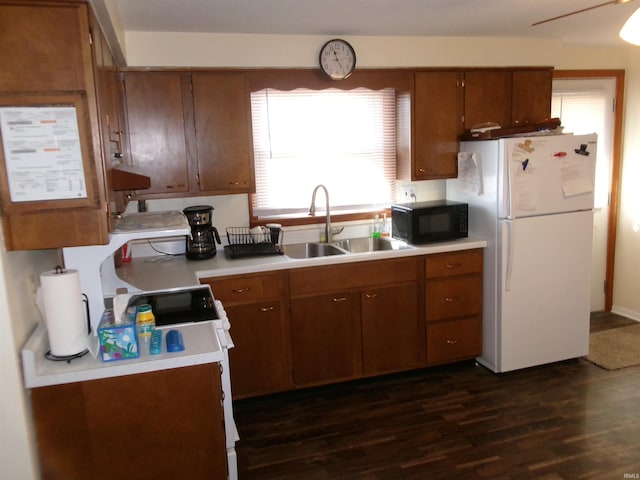 kitchen featuring dark wood-style flooring, freestanding refrigerator, a sink, light countertops, and black microwave