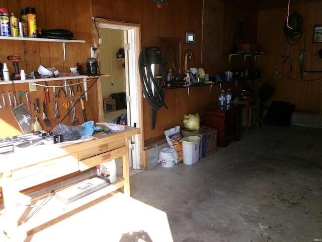 misc room featuring a workshop area, wood walls, and unfinished concrete floors