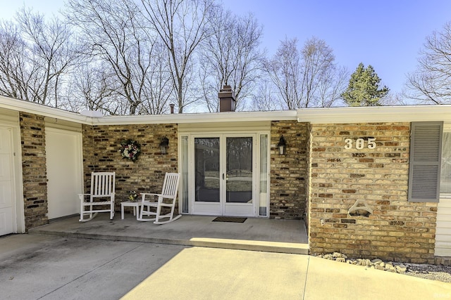 entrance to property with a garage, french doors, brick siding, and a chimney