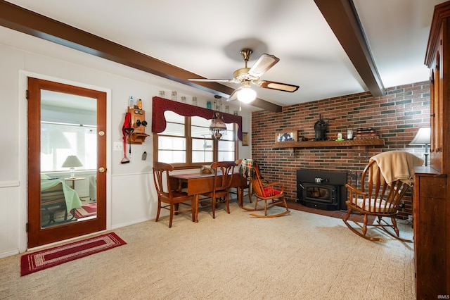 living area featuring beamed ceiling, a wood stove, carpet floors, and ceiling fan