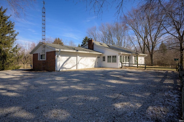 view of side of property with an attached garage, brick siding, gravel driveway, and a chimney