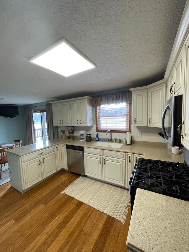 kitchen featuring a sink, wood finished floors, dishwasher, and a peninsula