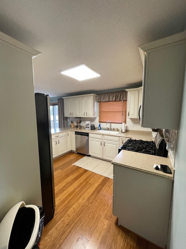 kitchen featuring light countertops, light wood-type flooring, appliances with stainless steel finishes, a textured ceiling, and a sink