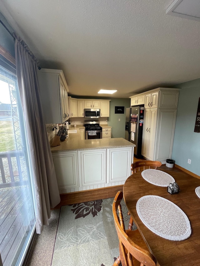 kitchen with light countertops, appliances with stainless steel finishes, a peninsula, a textured ceiling, and a sink