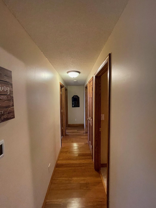 hallway with baseboards, light wood-style floors, and a textured ceiling