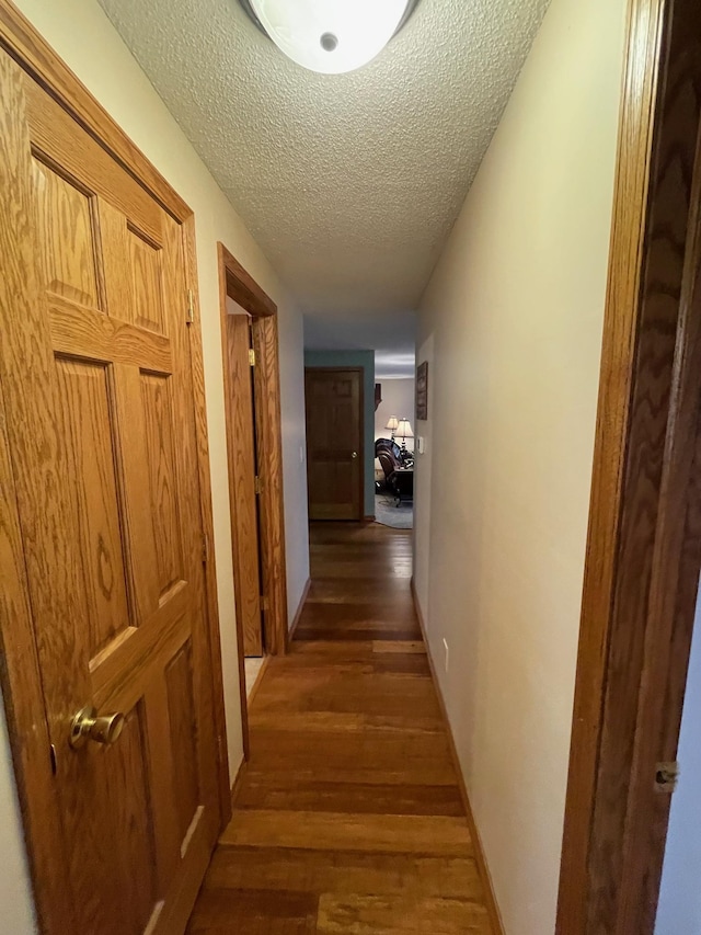 corridor with a textured ceiling, baseboards, and wood finished floors